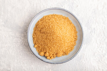 plate with unrefined golden cane sugar on gray concrete. top view, close up.