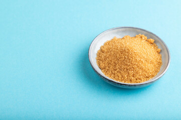 plate with unrefined golden cane sugar on blue pastel. side view, copy space.