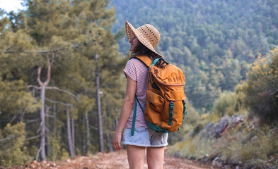 A woman with a backpack and a straw hat on a mountain path