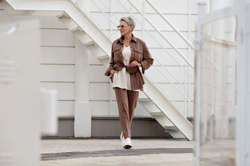 Stylish woman walking city street. Short hair Model wears beige business suit, belt purse, fashion...