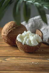 Pieces of organic coconut butter in a bowl and fresh coconut on a wooden table. Concept of healthy ingredient for cooking and natural cosmetics