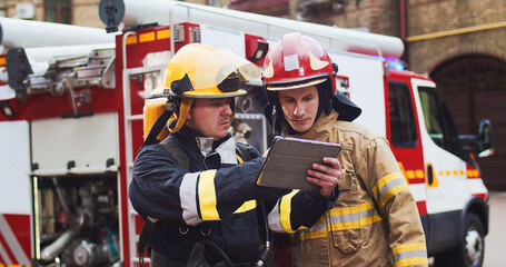 Medium plan of two firefighters discussing rescue plan looking at tablet while standing in helmets...