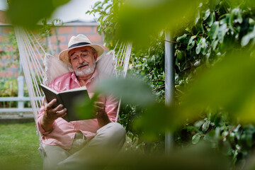 Happy senior man relaxing with book in his garden.