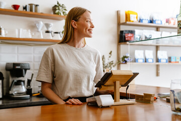 Blonde white barista woman working with tablet computer in cafe