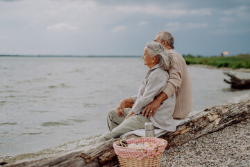 Senior couple sitting with picnic basket and having romantic moment near the autumn sea.