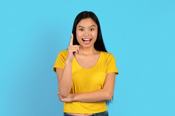 Glad inspired young japanese lady in yellow t-shirt with open mouth, show finger up on empty space,...