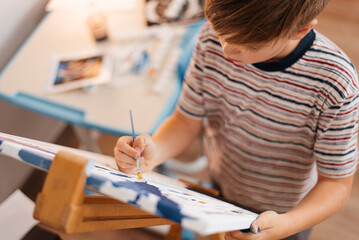 A boy paints a painting on canvas with a brush.