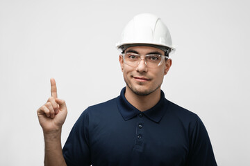 portrait of male engineer, architect, builder in white helmet pointing upward on white background,...