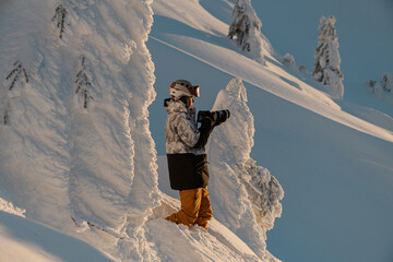 side view of male photographer with photo camera among snow-covered fir trees on mountain slope.