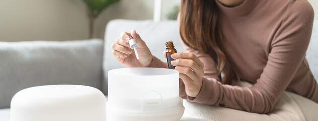 Women drop essential oil into the humidifier to make aromatherapy refreshments atmosphere house for relaxation. - obrazy, fototapety, plakaty