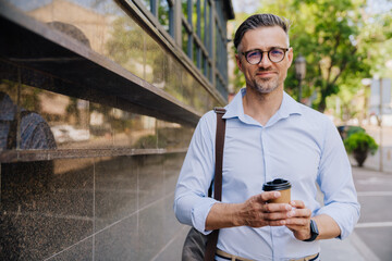 European grey man in eyeglasses drinking coffee outdoors