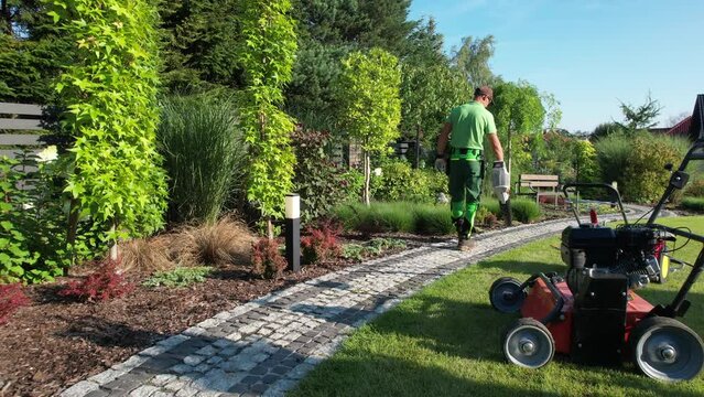 Caucasian Gardener Blowing Dirt and Leafs From Garden Cobble Paths