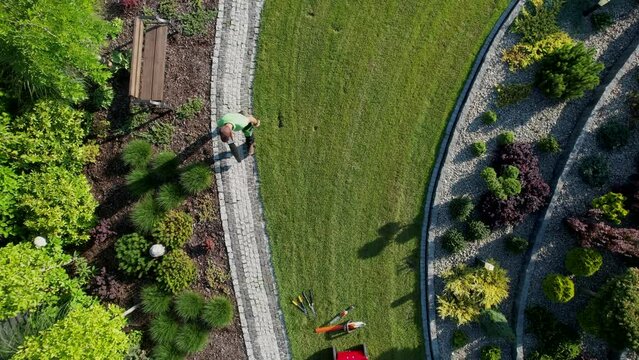 Aerial View of Gardener Blowing Dirt and Leafs From Garden Cobble Paths. Gardening and Landscaping Industry.