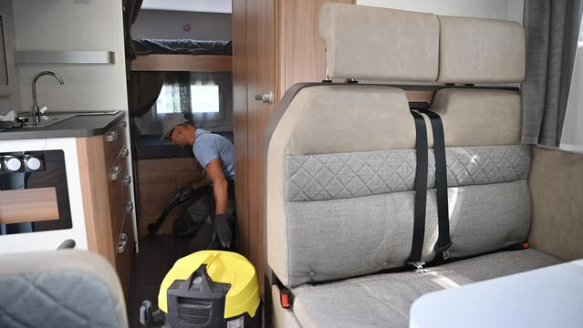 Caucasian Worker Cleaning Modern Recreational Vehicle RV Motorhome Interior Using Vacuum. Camper Van Maintenance.
