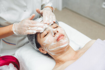 the cosmetologist cleanses the skin with foam. A woman's skin care procedure. Natural cosmetics. A beautiful face. Cosmetic treatment of the face. Therapeutic peeling cream.