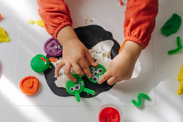 Child hands creating playdough funny monsters for the holiday of Halloween. Sensory play for...