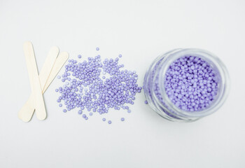 Close-up of lilac and pink wax granules scattered from a jar. Cosmetic procedure to remove unwanted...
