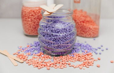Close-up of lilac and pink wax granules scattered from a jar. Cosmetic procedure to remove unwanted...