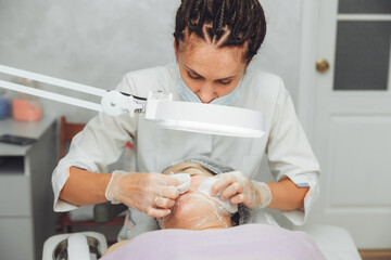 A cosmetologist in a beauty salon does a mechanical cleaning of a woman's face with his own hands. acne removal. heavily polluted face.