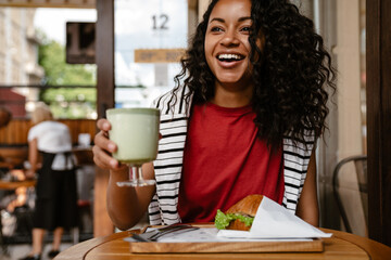 Young black woman smiling and having lunch while sitting at cafe