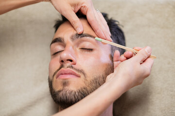 Crop beautician waxing eyebrows of male client - obrazy, fototapety, plakaty