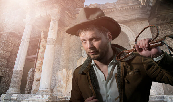 Young sexy unshaven man in cowboy hat. Romantic image of a vintage 

traveler and adventurer. like Indiana Jones. Man with a rope whip in his hand