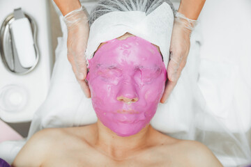 Care for the beauty of women's skin. A young woman with an alginate cosmetic purple mask on her...