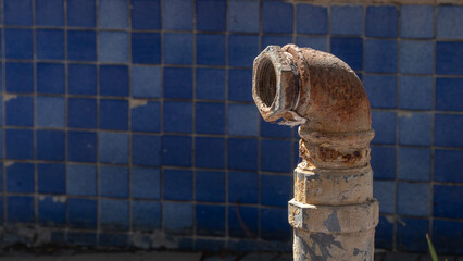 Metal rusty pipe on the background of blue facing tiles