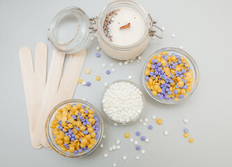 Beautiful granules of pink, white, yellow, blue wax for depilation in a glass bowl, wooden spatulas on a pink background. waxing. Epilation, depilation, removal of unwanted hair.