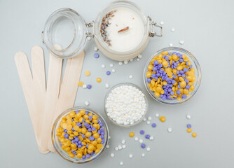 Beautiful granules of pink, white, yellow, blue wax for depilation in a glass bowl, wooden spatulas on a pink background. waxing. Epilation, depilation, removal of unwanted hair.