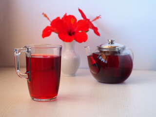 Hibiscus red tea in glass teapot, mug with tea, and fresh flowers