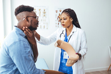 Obraz premium Doctor applying cervical collar on neck of African American man in clinic. Female doctor putting neck orthopaedic collar on adult injured man. Man in pain at the doctor for a neck injury