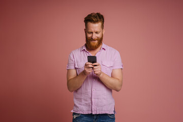 Ginger white man with beard smiling and using mobile phone