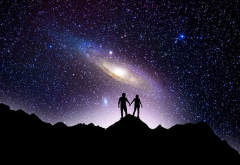  Fantasy night landscpe.Couple silhouette stands on the hill on and looks on the Andromeda galaxy. - obrazy, fototapety, plakaty