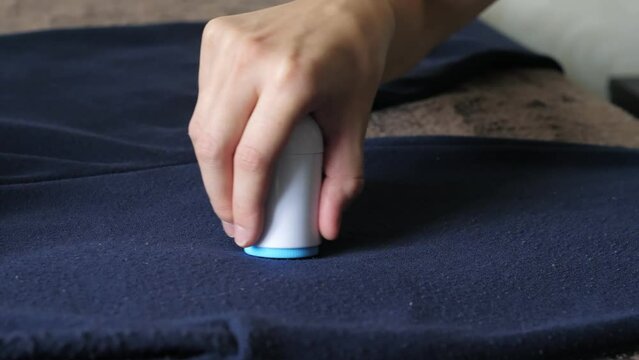 Womans hand, holding a machine for removing pellet and pools from clothes and fabric, uses on a dark blue knitted men's pants. A modern electronic device for updating old things. Textile care concept.