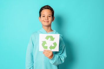 Child boy holding recycling symbol paper standing isolated over green background.. Recycling...