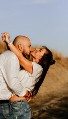 Happy smiling  Couple walking at Sand Dunes near the Beach.  Young happy Bearded muscular  man  in White shirt kissing and hugging beautiful woman at sunser on a beach