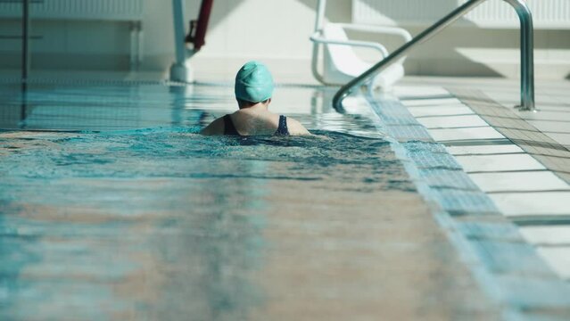 A young woman swims breaststroke in the pool cutting through the water with her hands. Front view. Slow motion
