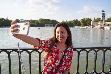 attractive latina taking a selfie in the retiro park in madrid. Young tourist visiting madrid - obrazy, fototapety, plakaty