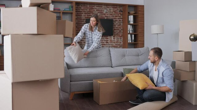 Young couple unpacking cardboard box and discussing interior design in new apartment on moving day. Happy homeowners on relocation day. Real estate and tenancy concept. Loan mortgage for young family.