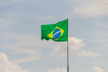Bandeira do Brasil voando e tremulando ao vento com céu nublado ao fundo.