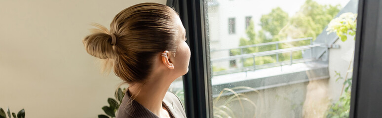 Young woman looking at balcony door at home, banner.