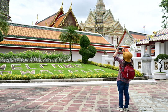 A female traveler uses a mobile phone to take pictures of the beauty of the pagodas and lawns with "WELCOME TO WATPHO" signs in famous temples: Wat Pho or the Reclining Buddha Temple in Bangkok.
