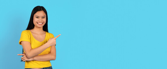 Cheerful young chinese female in yellow t-shirt points finger at empty space, recommend ad