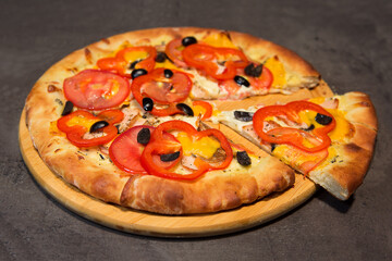 Appetizing pizza with cut off piece on a wooden stand on a black concrete background. Top view.	