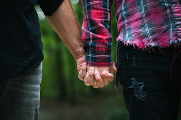 Gay couple holding hands outdoor, close up. Homosexual partners walking together.