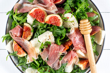 Salad with arugula , figs, prosciutto and mozzarella on white wooden background