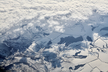 Aerial cloudscape view over clouds top to snow covered rivers, roads, cities and fields, winter air