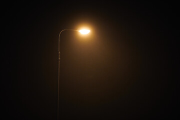 One night lamppost shines with faint mysterious yellow light through evening fog, copy space