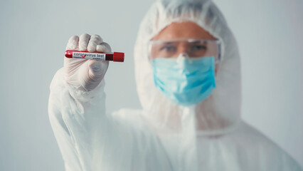 blurred doctor in hazmat suit showing negative coronavirus test isolated on grey.